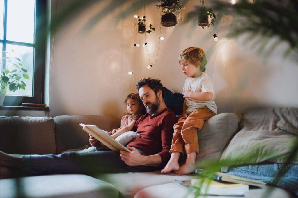 Vater liest auf der Couch seinen Kindern ein Buch vor, dank der gewonnenen Zeit durch eine Reinigungskraft in Hamm