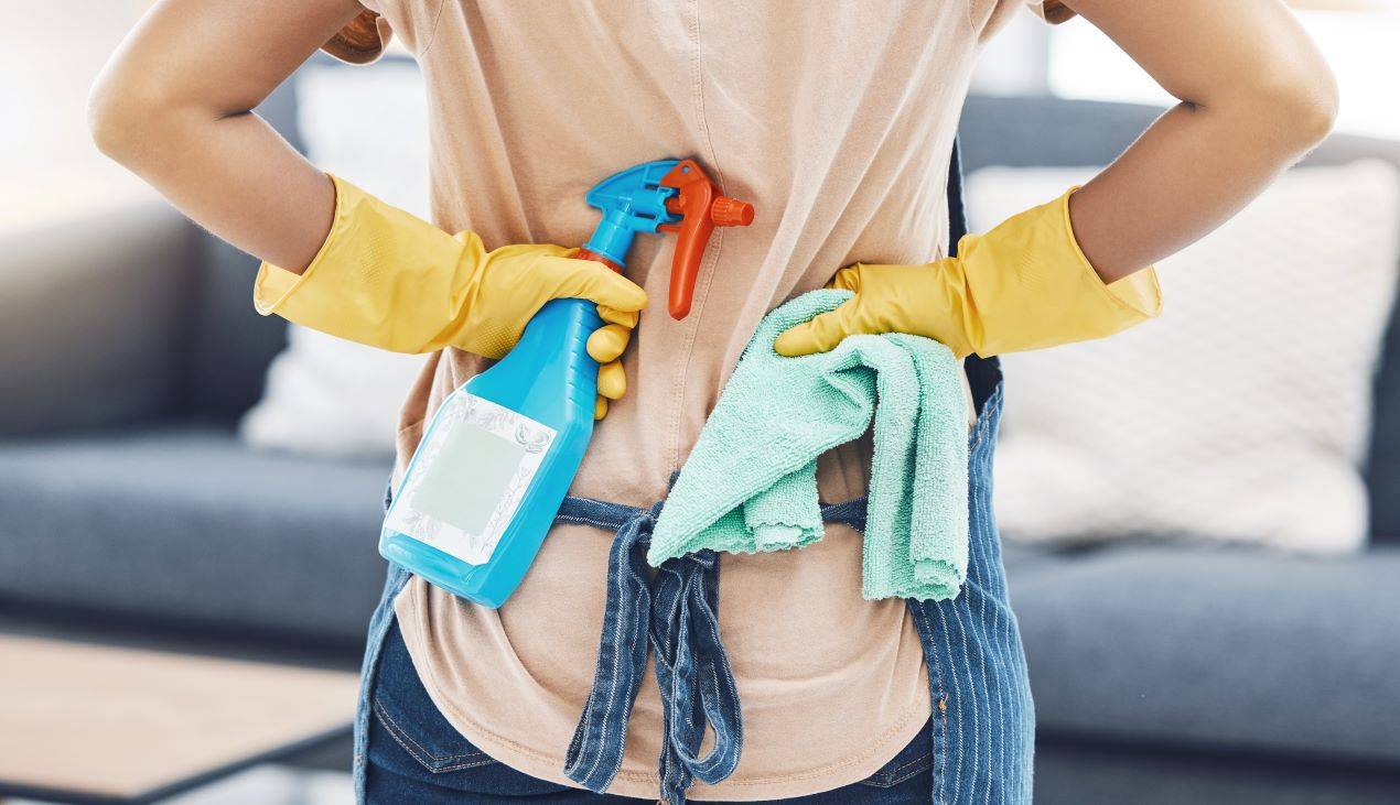 Reinigungskraft in Hamm mit gelben Handschuhen, Reinigungsspray und Mikrofasertuch, bereit für die Reinigung eines Wohnzimmers